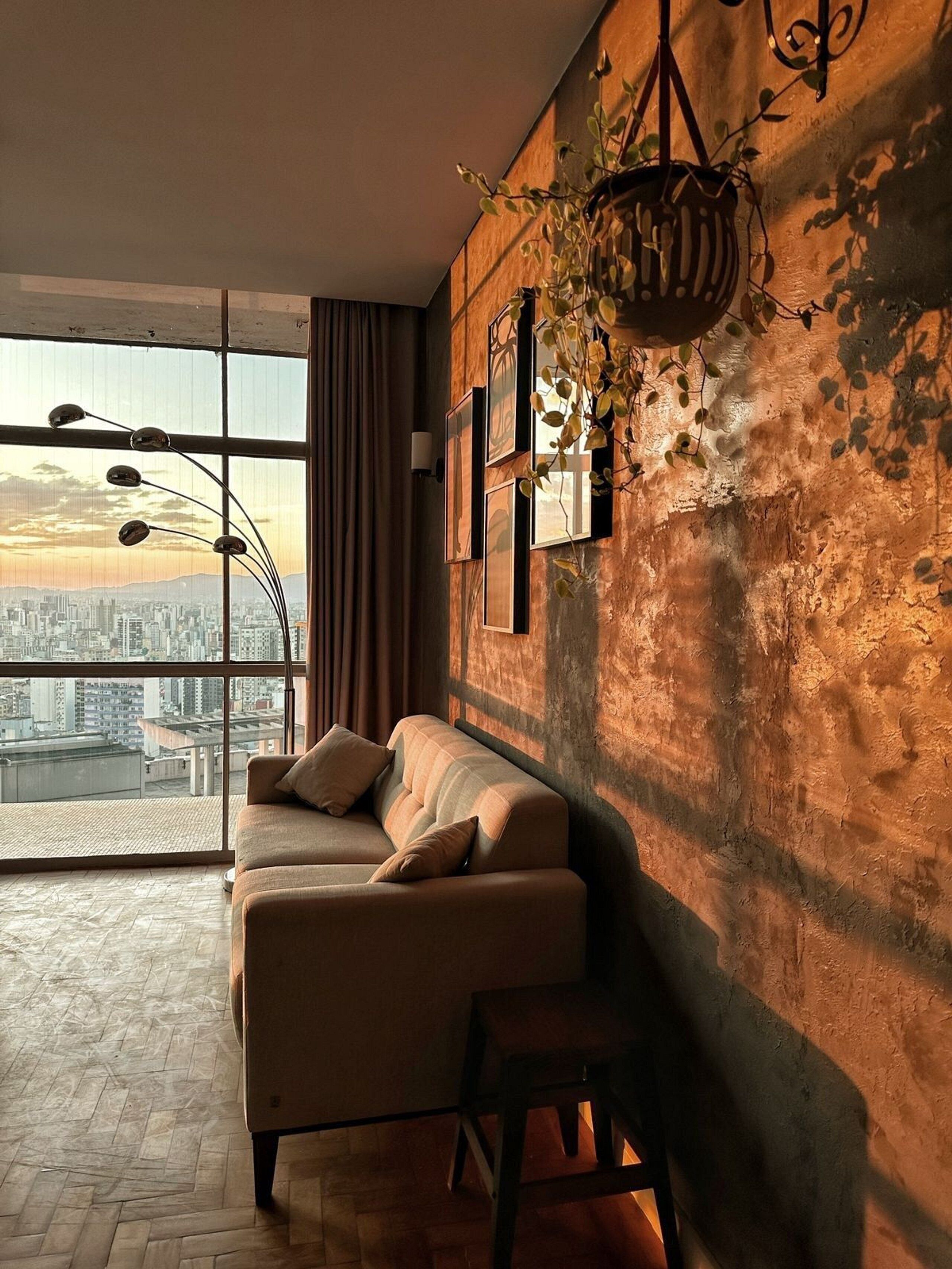 Ein modernes Wohnzimmer mit großem Fenster, einer Couch, einer hängenden Pflanze und Blick auf die Stadt.