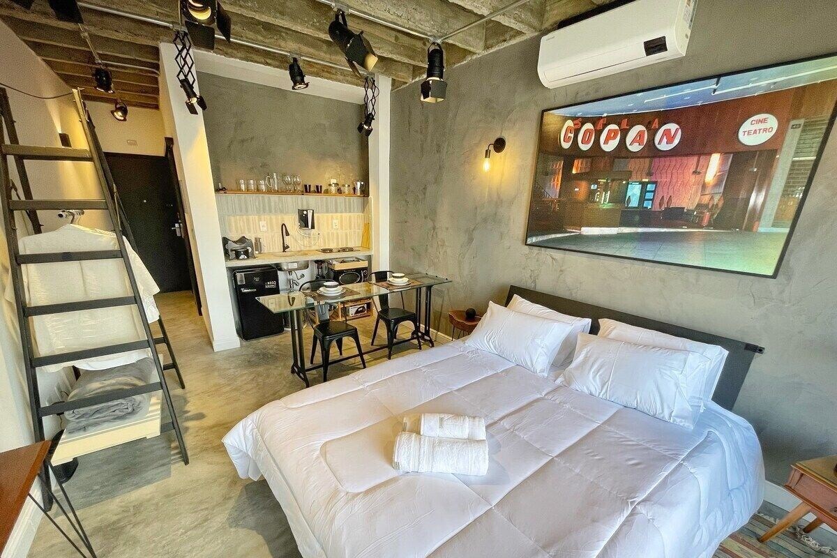 Ein Hotelzimmer mit einem großen Bett, einem Schreibtisch mit Stühlen, einer Küchenzeile und Blick auf ein Kino.