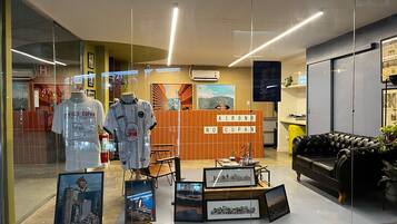 Un vestíbulo de hotel con una recepción, un sofá de cuero negro, cuadros con vistas de la ciudad y dos maniquíes mostrando camisetas deportivas.