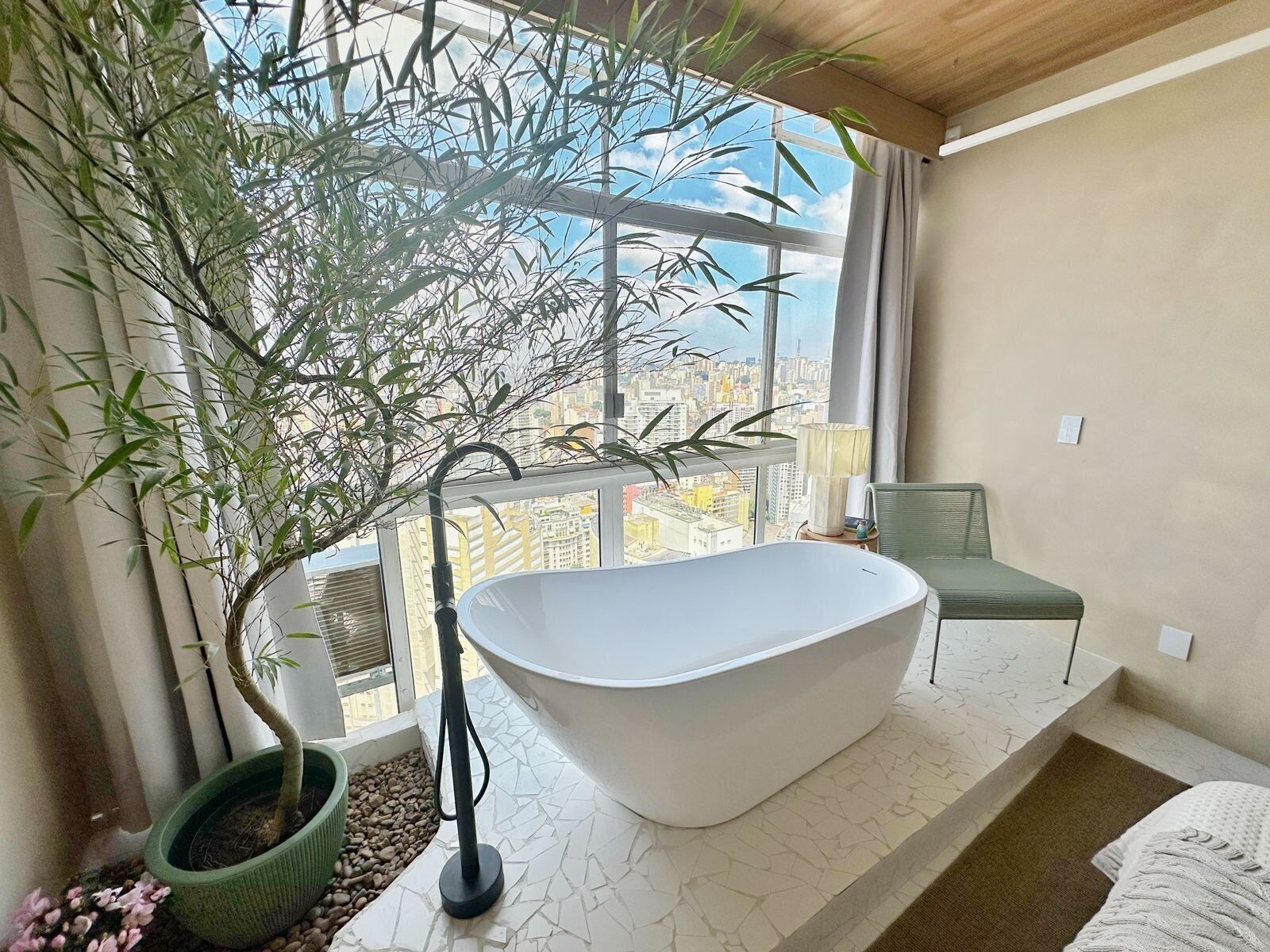 Ein modernes Badezimmer mit einer freistehenden Badewanne, einer Topfpflanze und Blick auf die Stadt durch große Fenster.