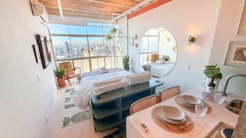 Una habitación de hotel moderna con vista a la ciudad, una cama, un área de comedor y un baño.