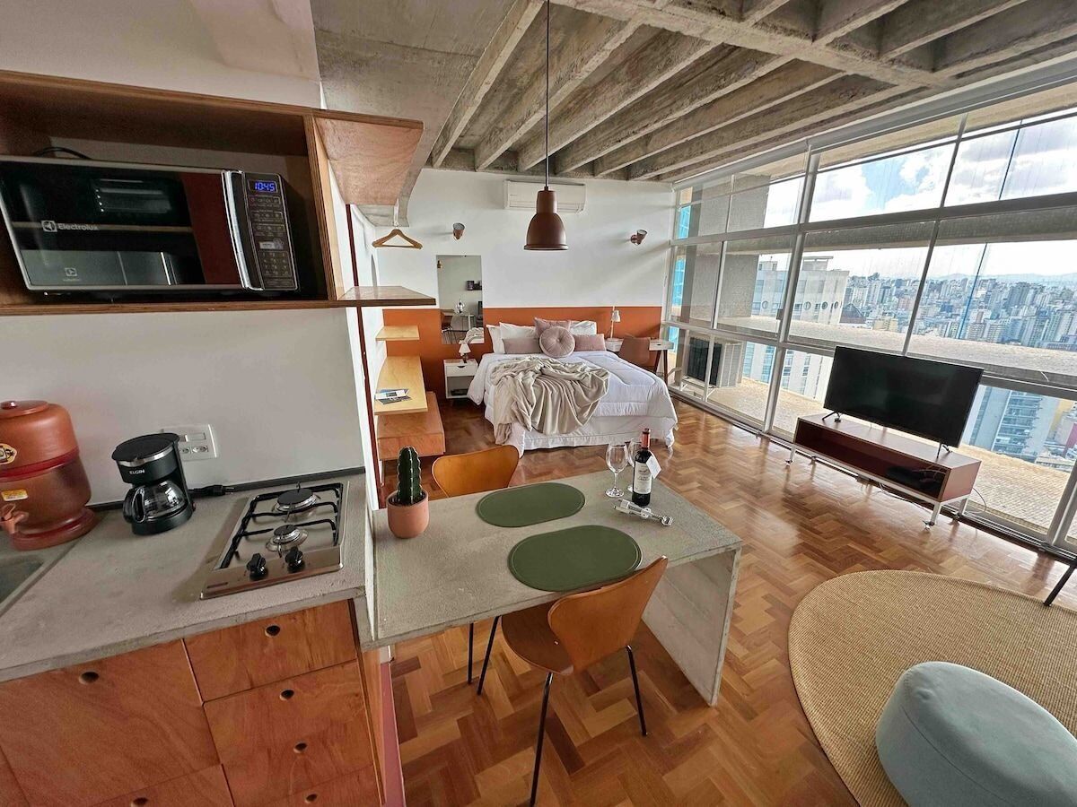 Une cuisine moderne équipée d’un four à micro-ondes, d’une machine à café et d’une cuisinière à gaz. On y trouve également un coin repas avec une table et des chaises, ainsi qu’une grande fenêtre donnant sur la ville.