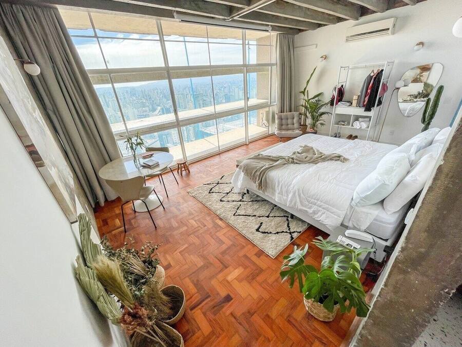 Een moderne slaapkamer met een groot bed, een klein bureau en uitzicht op de stad door grote ramen.