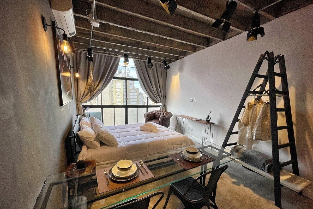 Une chambre d’hôtel de taille réduite, avec un lit, une table à manger en verre et une échelle appuyée contre le mur.