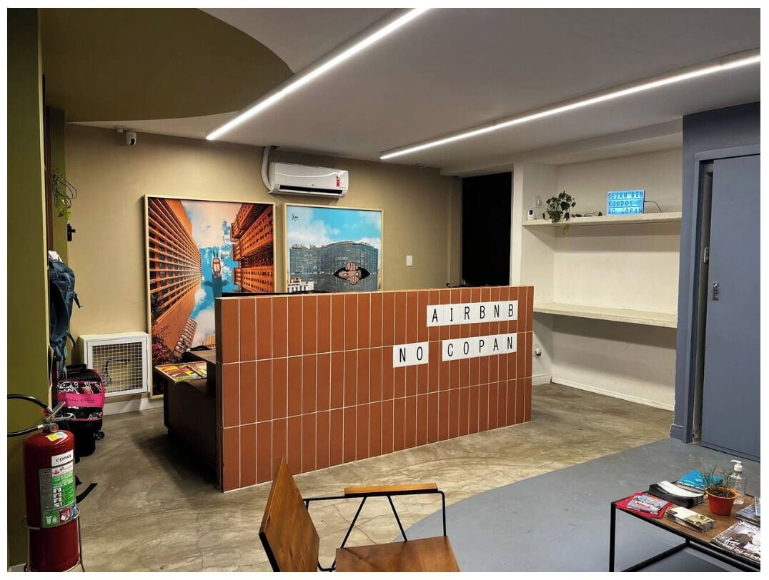 A reception desk with a sign reading "AIRBNB NO COPAN" and a cityscape painting on the wall.