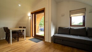 A room with a wooden floor, a gray sofa, a dining table with chairs, and a door leading outside. - 2 Cosy Cabin at 15th C Pub (Wendens Ambo)