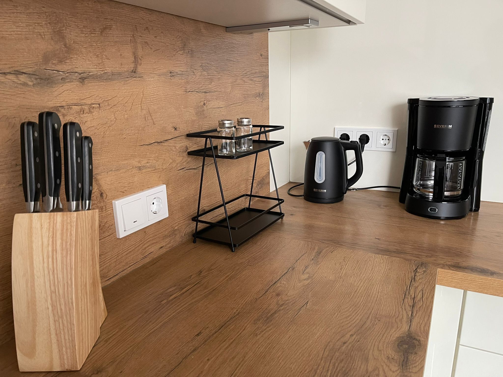 A kitchen with a wooden countertop, a knife block, a black coffee maker, and a black kettle.