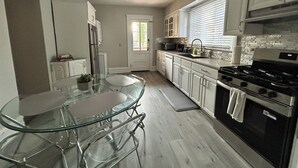 Une cuisine moderne avec des meubles blancs, une table à manger en verre et une cuisinière en acier inoxydable.