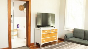 Um quarto com cama, televisão sobre um penteadeira, sofá e janela com persianas.