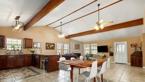 A spacious kitchen with wooden beams, a dining area with a large table and chairs, and a living room with a TV and seating. - NEW Artist's Retreat on 11 Acres, Pet-Friendly, Dark Skies, Nature Escape, Fire Pit, Games, Grill (New Braunfels)