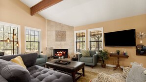 A living room with a fireplace, sofas, a coffee table, and a TV mounted on the wall. - NEW Artist's Retreat on 11 Acres, Pet-Friendly, Dark Skies, Nature Escape, Fire Pit, Games, Grill (New Braunfels)