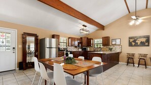 A spacious kitchen with wooden cabinets, a stainless steel refrigerator, and a dining area with a wooden table and white chairs. - NEW Artist's Retreat on 11 Acres, Pet-Friendly, Dark Skies, Nature Escape, Fire Pit, Games, Grill (New Braunfels)
