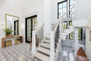 Un escalier avec des rampes blanches et des balustres noires, menant à un palier agrémenté d’un grand miroir et d’une console.