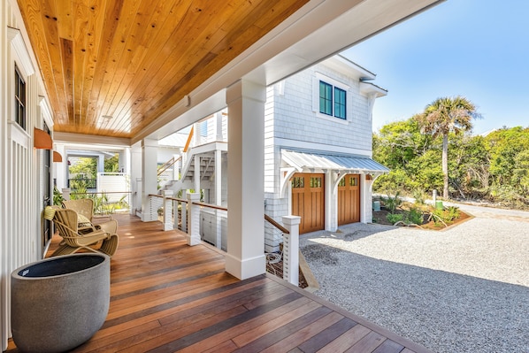 A covered porch with wooden flooring, white columns, and a view of a house with a white exterior and blue windows. - LUXURY! 6 BR Sky Watch Views 2 Min Walk to E. Beach Shoals Club - 4 day min stay (Bald Head Island)