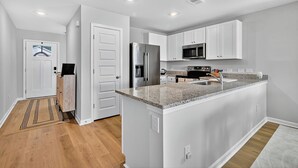 A modern kitchen with white cabinetry, a granite countertop, stainless steel appliances, and a central island. - Family Fun w/Game Rm, WFH Office: 8 Min to Beach (Ocean Isle Beach)