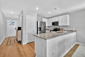 A modern kitchen with white cabinetry, a granite countertop, stainless steel appliances, and a central island. - Family Fun w/Game Rm, WFH Office: 8 Min to Beach (Ocean Isle Beach)