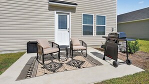 A patio with two chairs and a grill, a door, and windows on a house. - Family Fun w/Game Rm, WFH Office: 8 Min to Beach (Ocean Isle Beach)