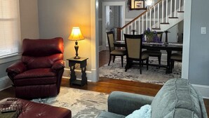 A living room with a red leather chair, a grey sofa, a small table with a lamp, and a staircase leading to a dining area. - The Wisteria House invites you to relax and enjoy! (Shelby)