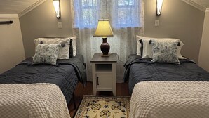 A bedroom with two beds, a nightstand, a lamp, a window with curtains, and a patterned rug. - The Wisteria House invites you to relax and enjoy! (Shelby)