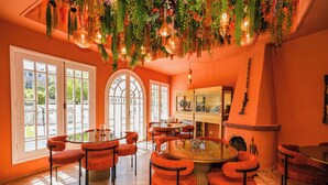 A dining area with a round table and orange chairs, surrounded by large windows and a decorative ceiling. - Palais Elya (Rabat)