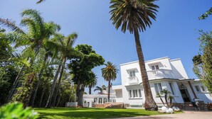 A white building with a symmetrical facade, surrounded by palm trees and a well-maintained lawn. - Palais Elya (Rabat)