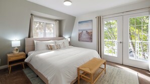 Une chambre avec un grand lit, une table de chevet, un banc, un tableau et une vue sur la verdure par la porte.