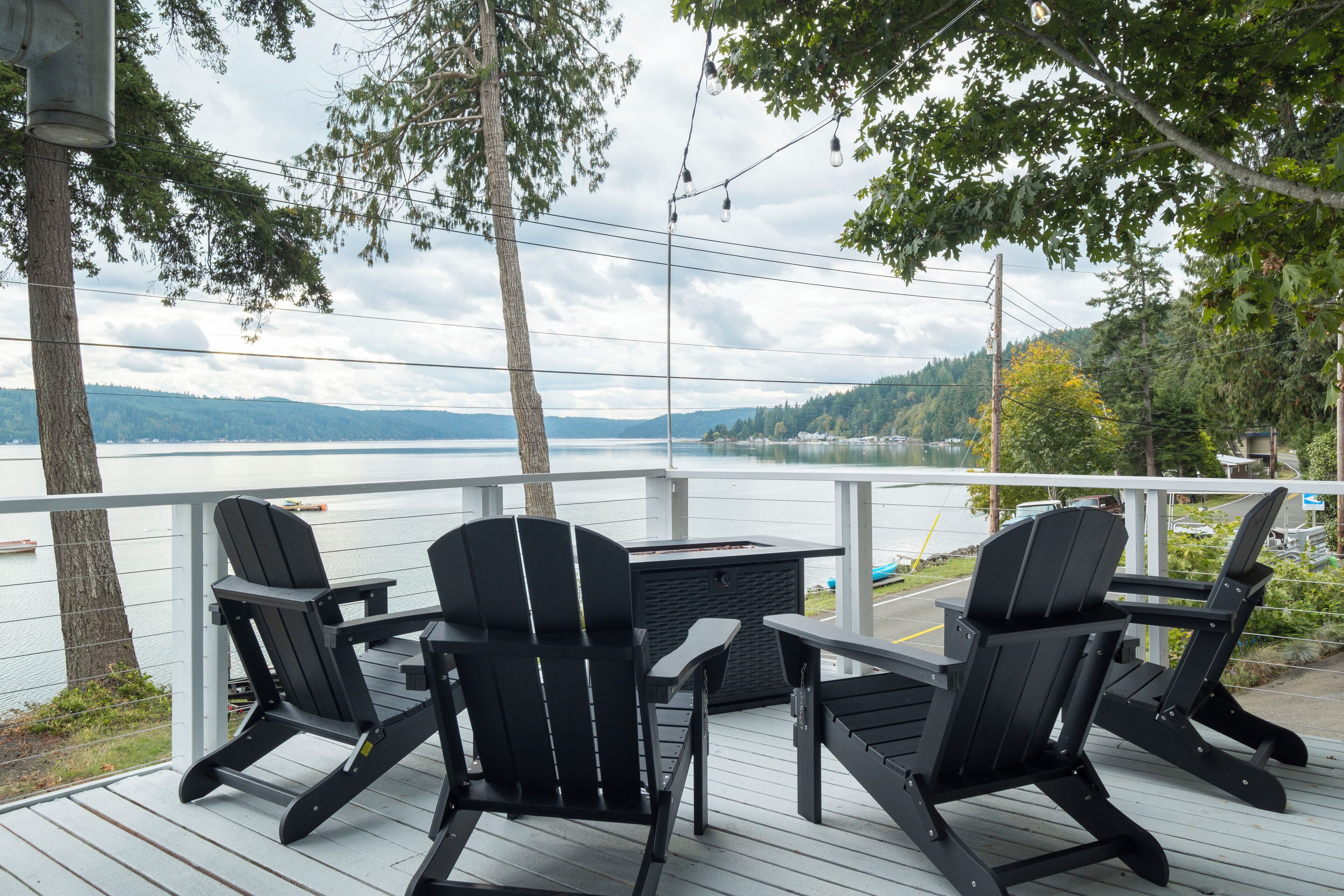 A deck with Adirondack chairs and a table overlooking a lake.