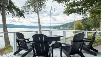 A deck with Adirondack chairs and a table overlooking a lake.