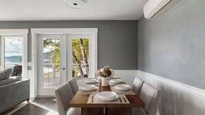 Un coin repas avec une table en bois dressée pour six personnes, entourée de chaises, et donnant sur l’extérieur grâce à une porte vitrée.