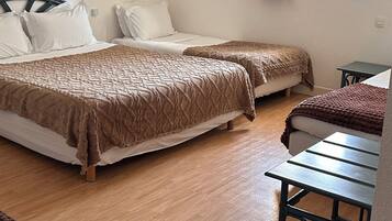 A room with two beds, a table, a window with curtains, and a wall-mounted picture.