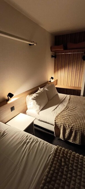 A hotel room with a bed, bedside tables, a lamp, and a window with blinds. - Hôtel du Rocher (Le Caylar)