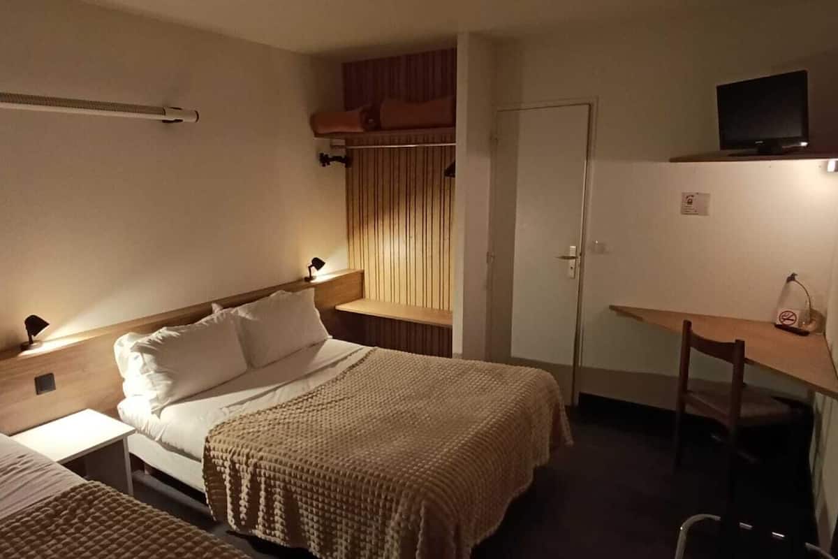 A hotel room with two single beds, a desk, a chair, and a television on a shelf.