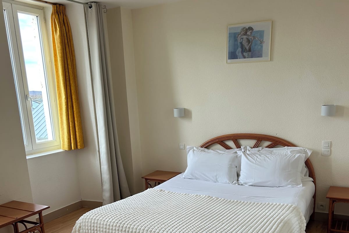 A bedroom with a bed, bedside tables, a window with curtains, a painting on the wall, and a wooden floor.
