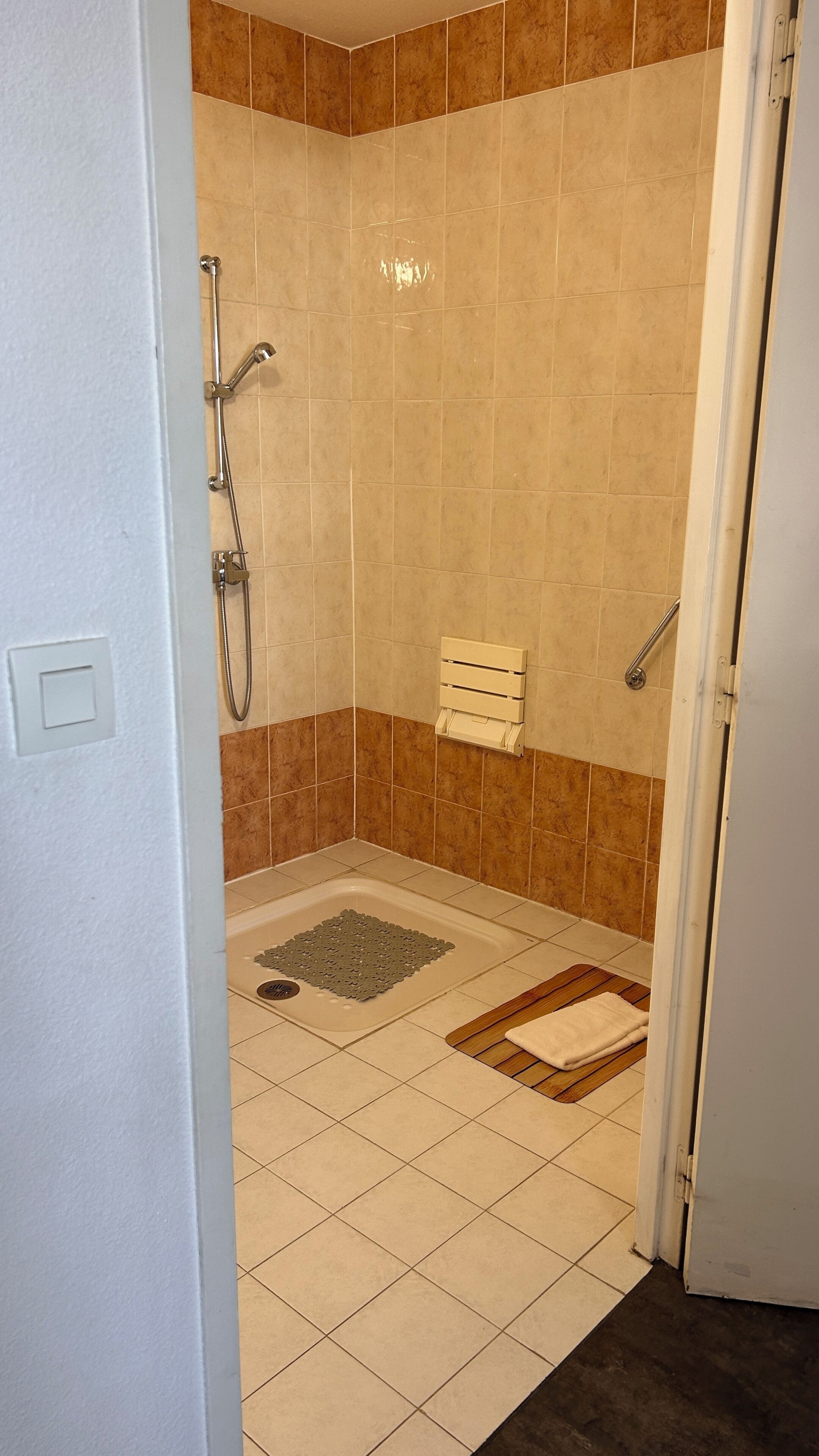 A bathroom with a shower, a towel rack, and a mat.