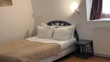 Un dormitorio con cama, una mesita, un radiador y una ventana con cortinas.