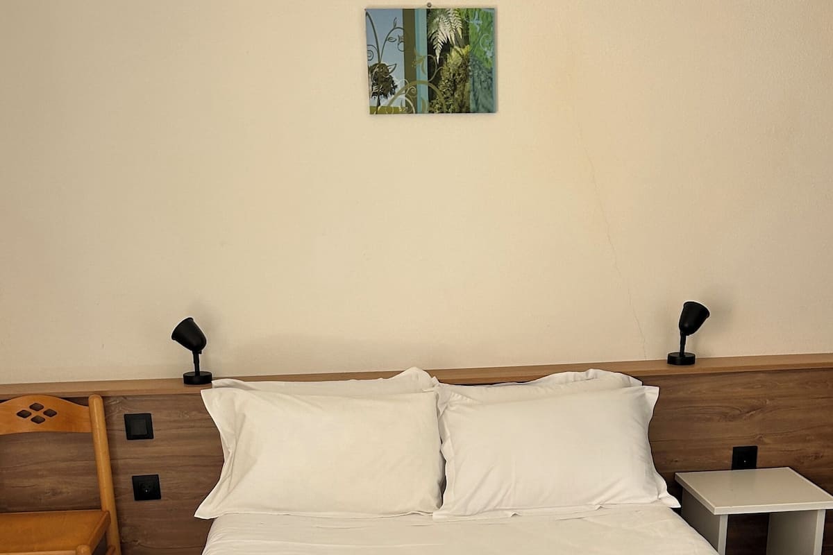 A neatly made bed with white and brown bedding, a wooden headboard, a small bedside table with a lamp, and a wall-mounted picture.