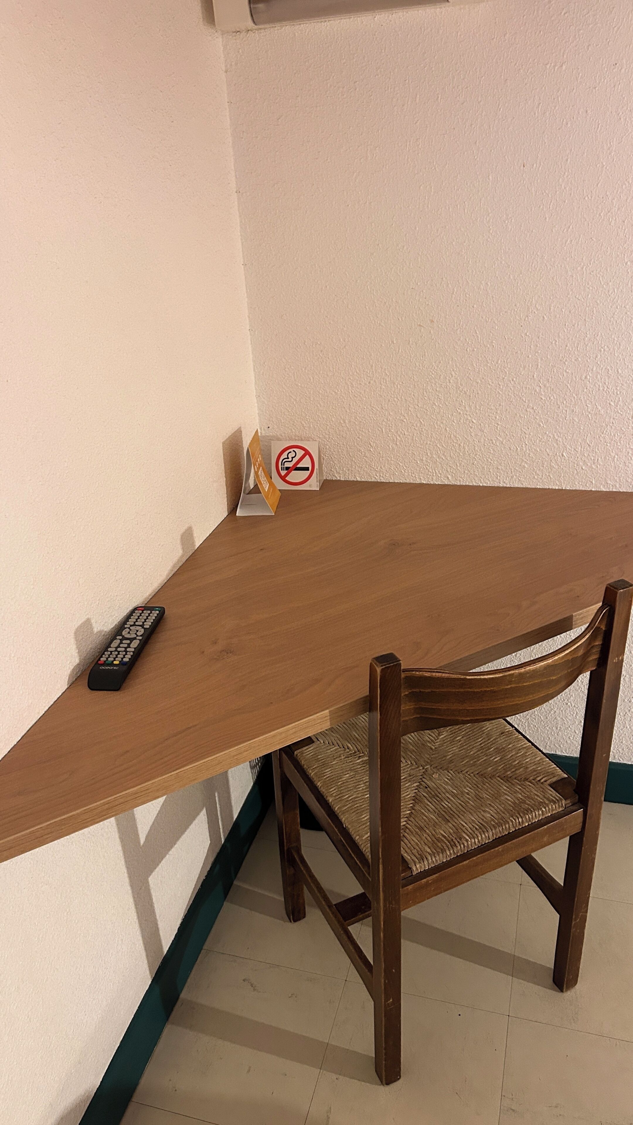 A corner table with a remote control, a no-smoking sign, and a woven chair.