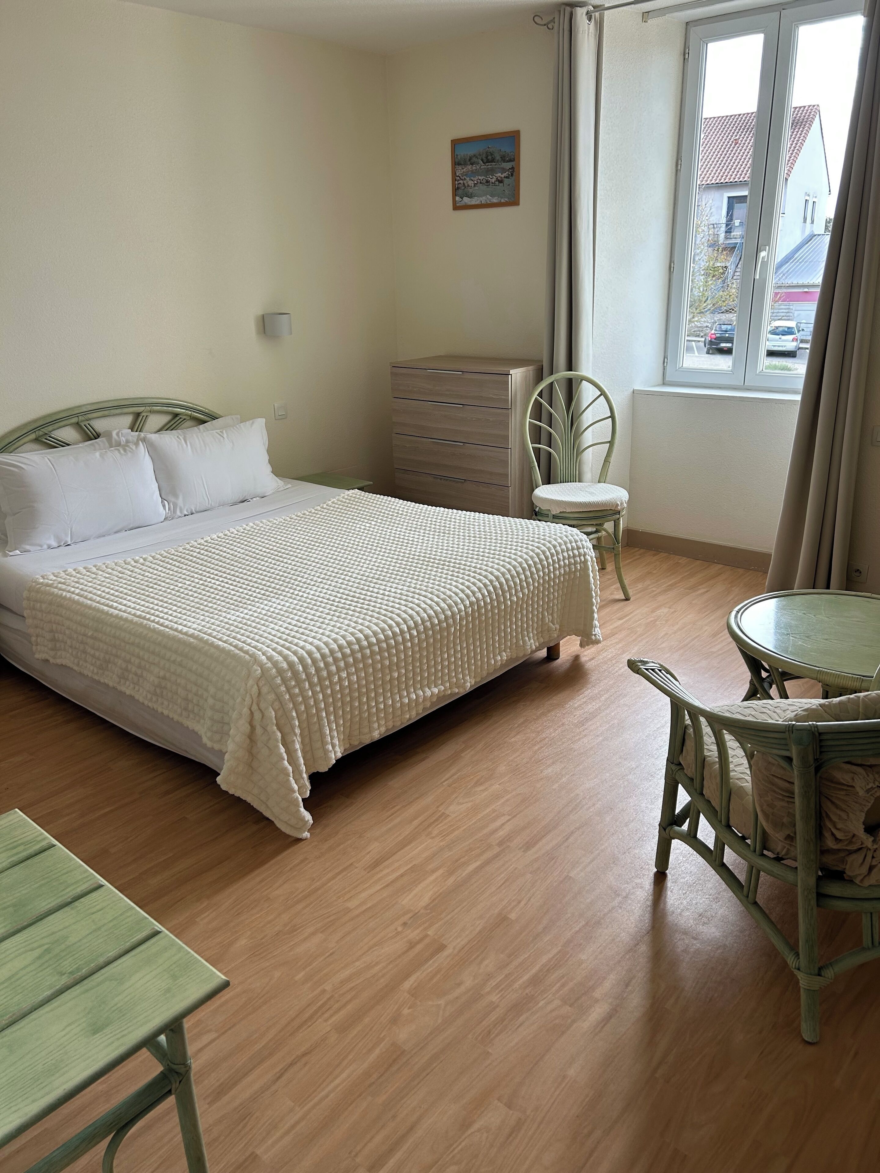 Une chambre à coucher comprenant un lit, une commode, une chaise, une table et une fenêtre donnant sur l’extérieur.