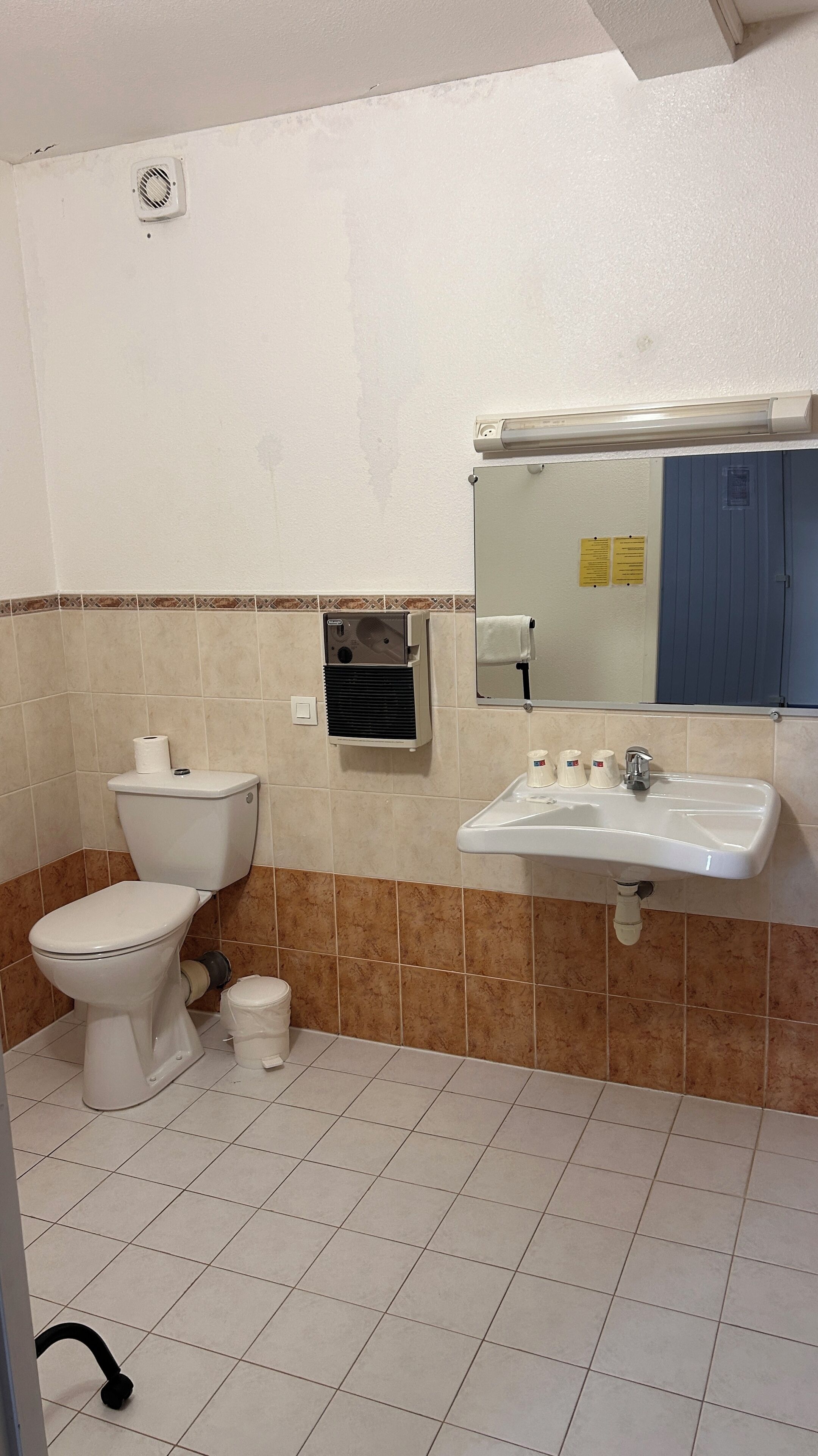 A bathroom with a toilet, sink, mirror, and tiled walls.