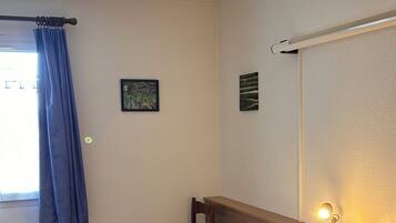 A hotel room with a bed, a chair, a desk, a window with curtains, and a wall-mounted lamp.