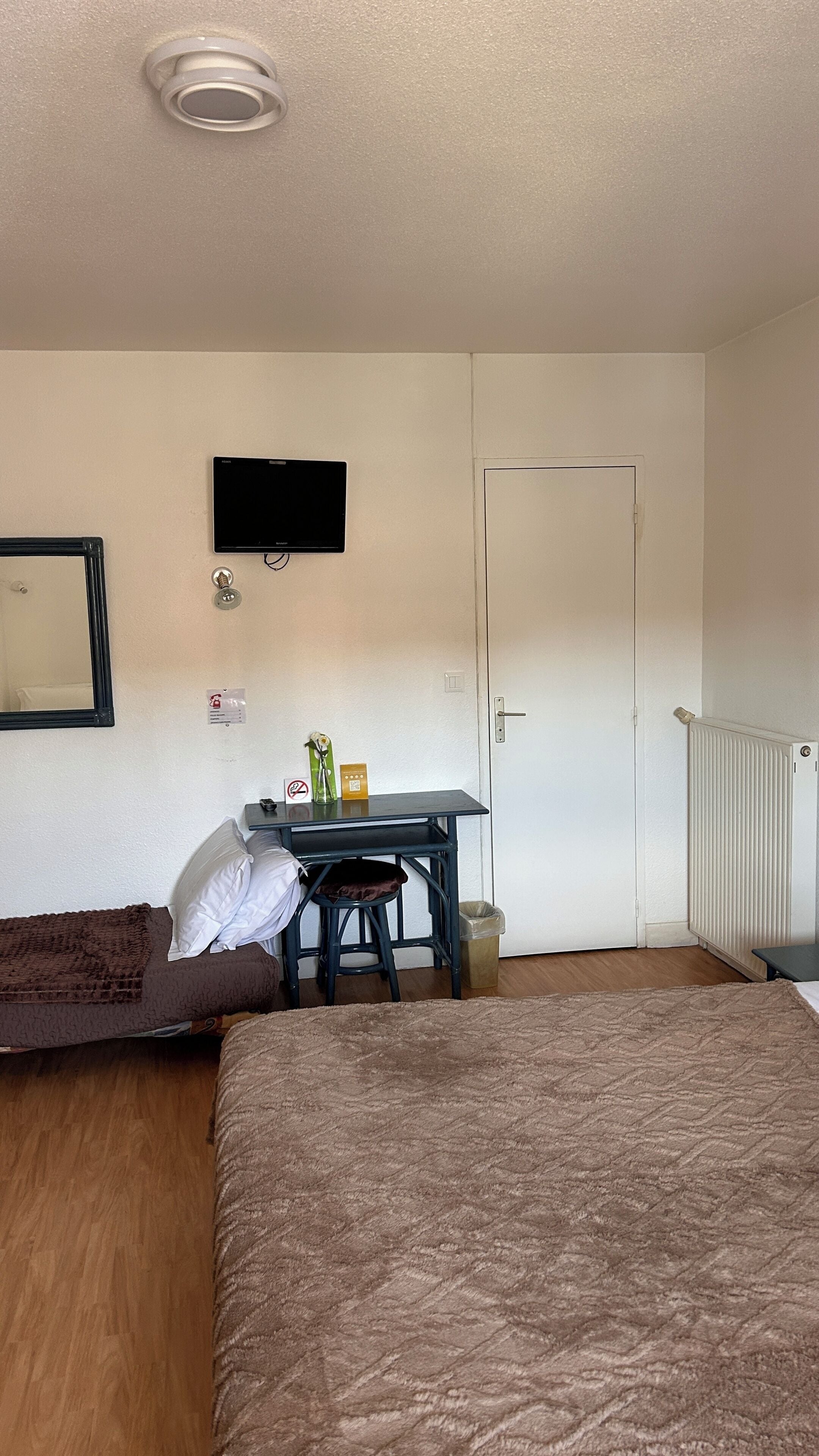 Une pièce comprenant un lit, un bureau, une chaise, un téléviseur, une porte et un radiateur.