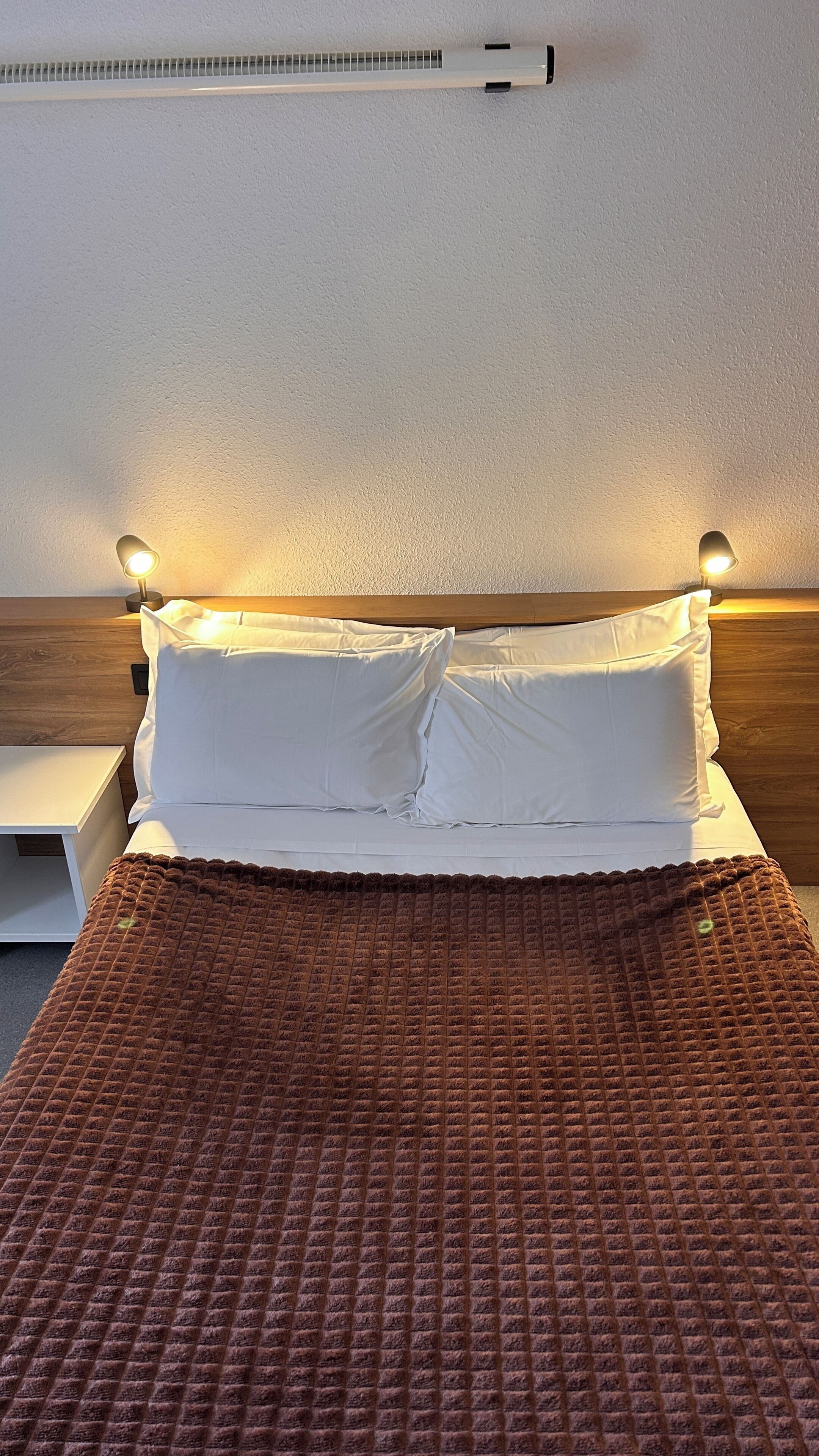 A bed with white linens, a brown textured blanket, and two bedside lamps.