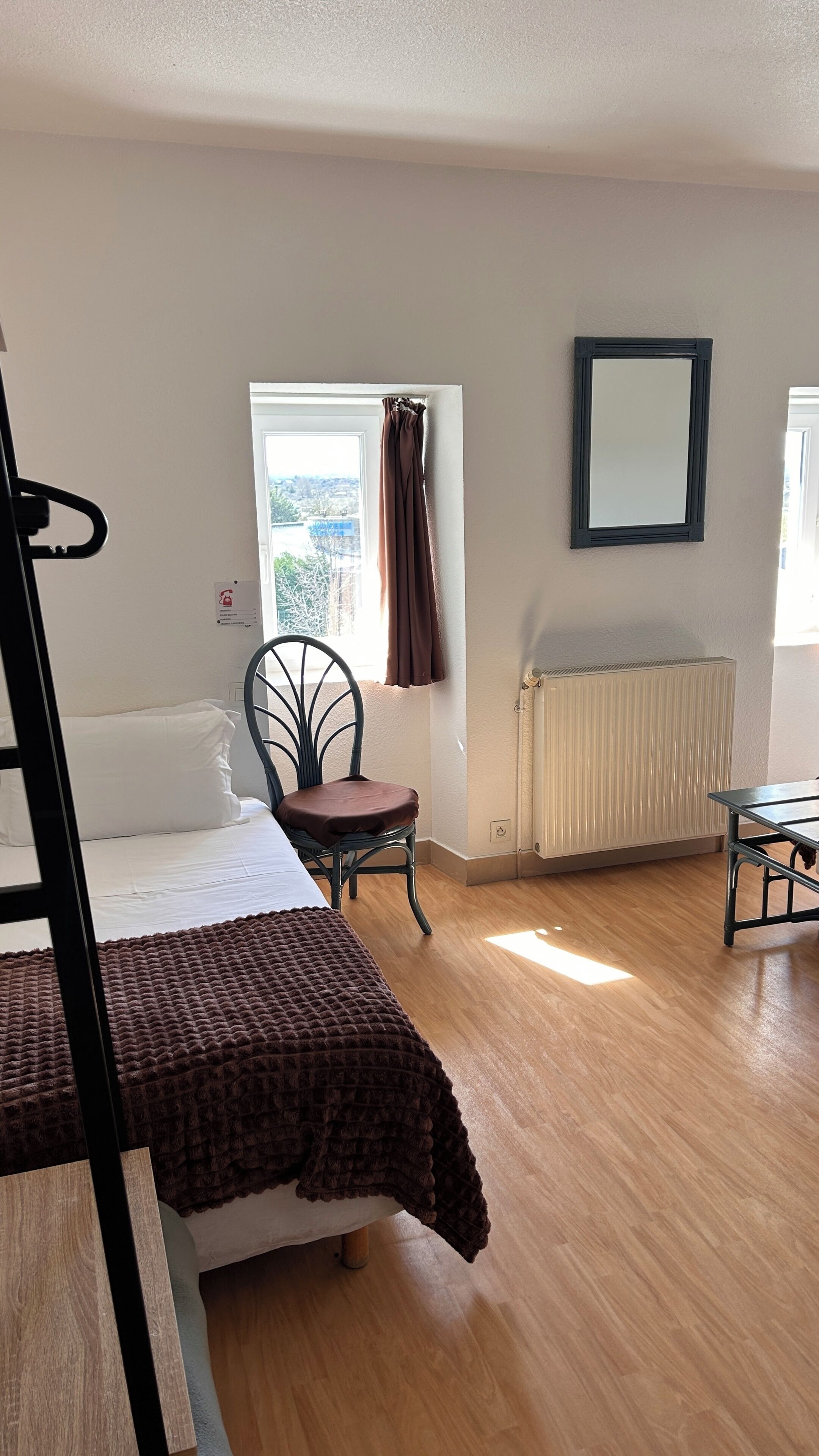 Quarto com cama, cadeira, radiador e janela com cortinas.