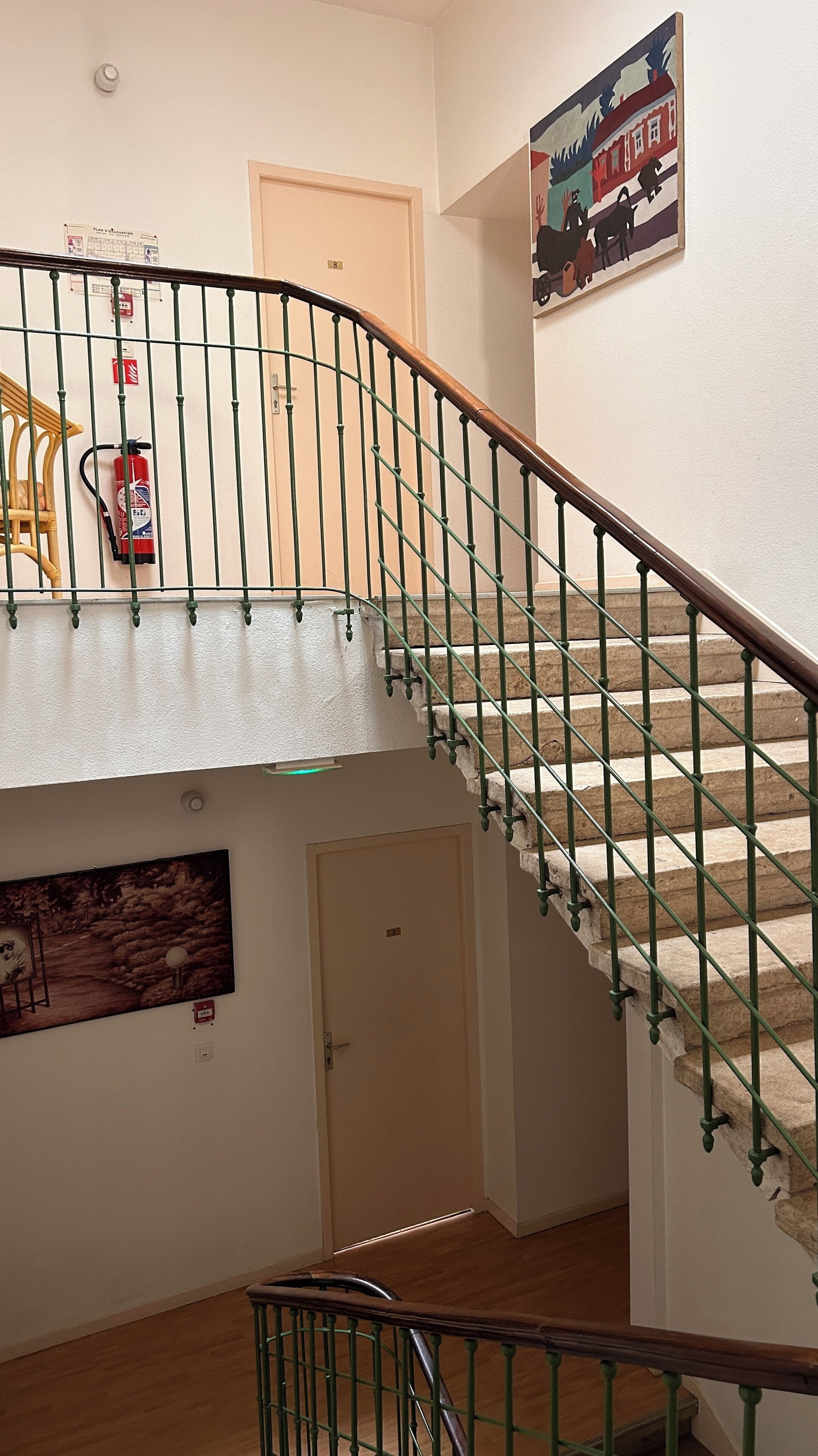 Una escalera con barandillas verdes, un extintor, una puerta y un cuadro en la pared.