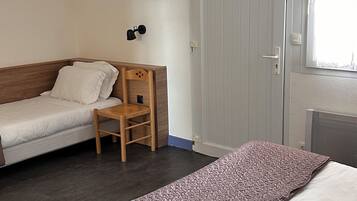 Una habitación con dos camas individuales, una silla de madera, un escritorio, una puerta blanca y una ventana.