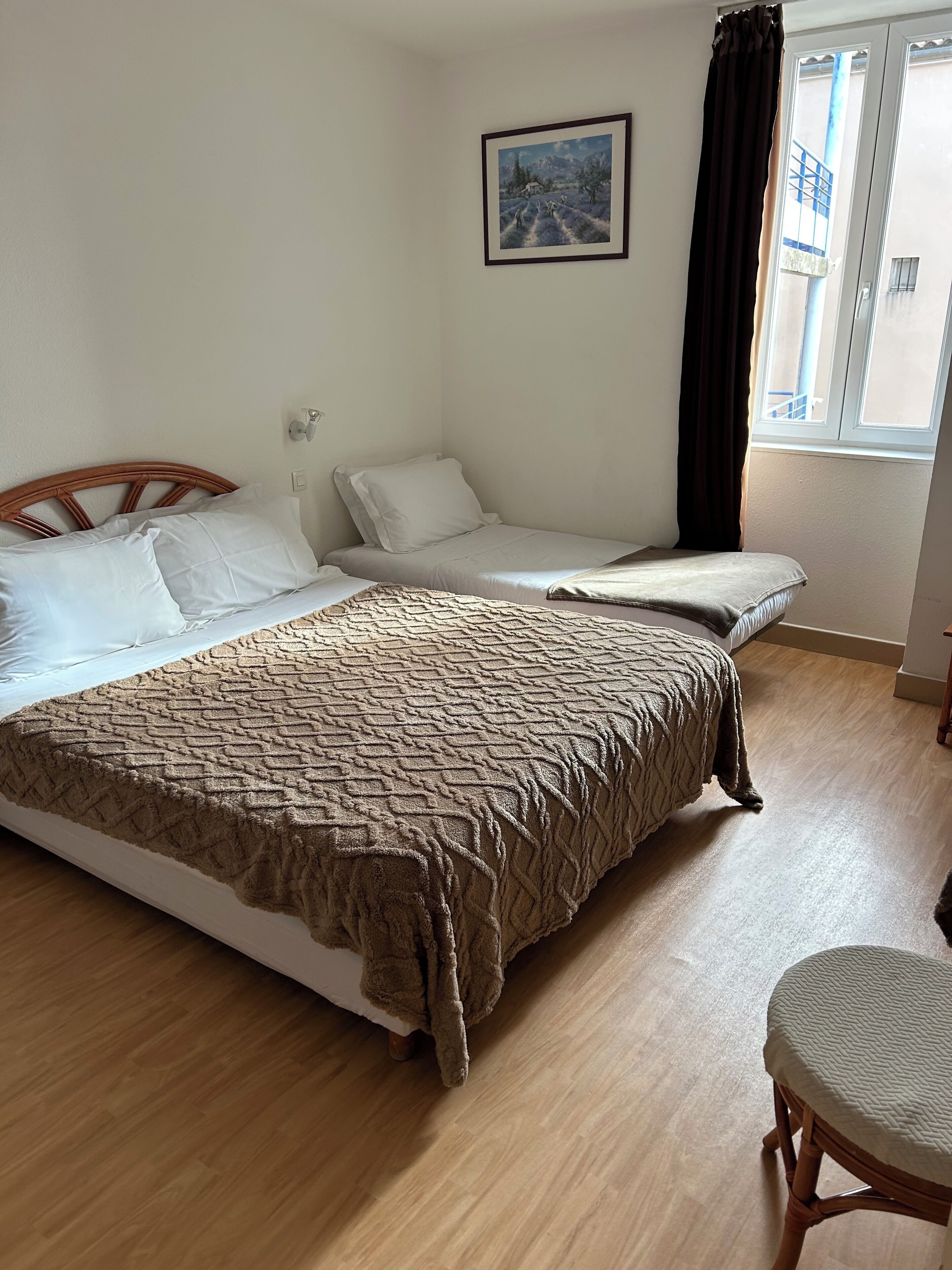 A room with a large bed, a smaller bed, a chair, a painting on the wall, and a window with curtains.