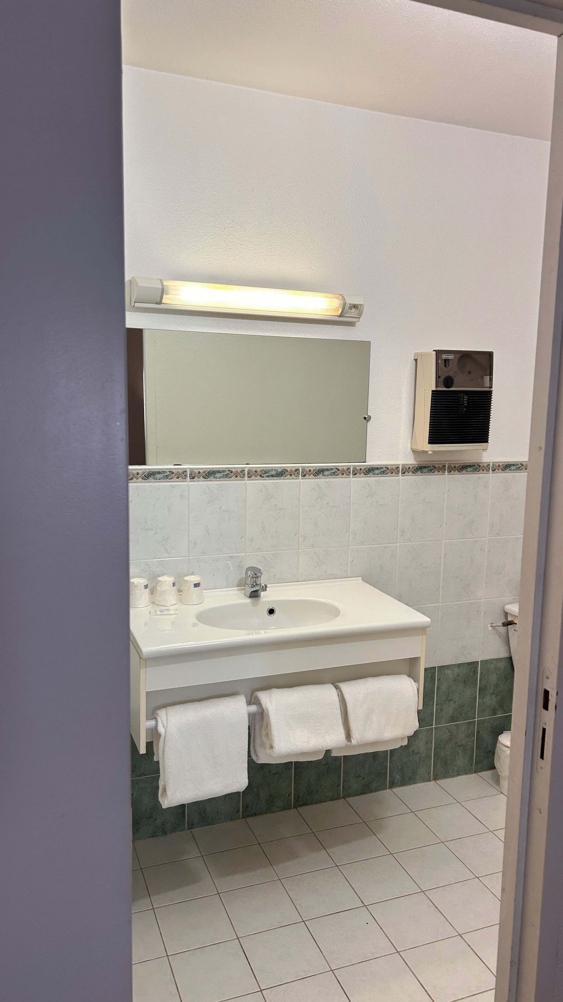 A bathroom with a white sink, mirror, and green-tiled walls.