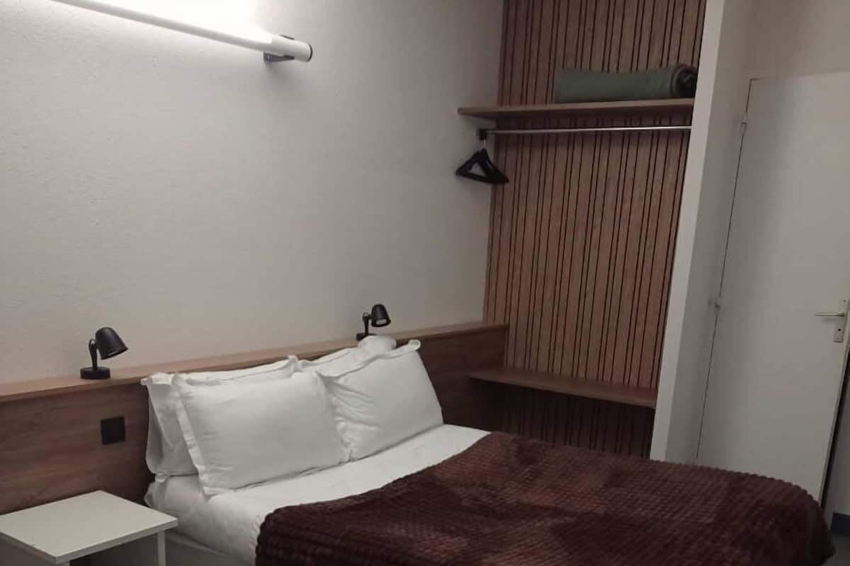 A hotel room with a bed, bedside tables, a wardrobe, and a hanging shelf.