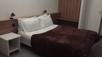 Een hotelkamer met een bed, nachtkastjes, een garderobe en een hangplank.