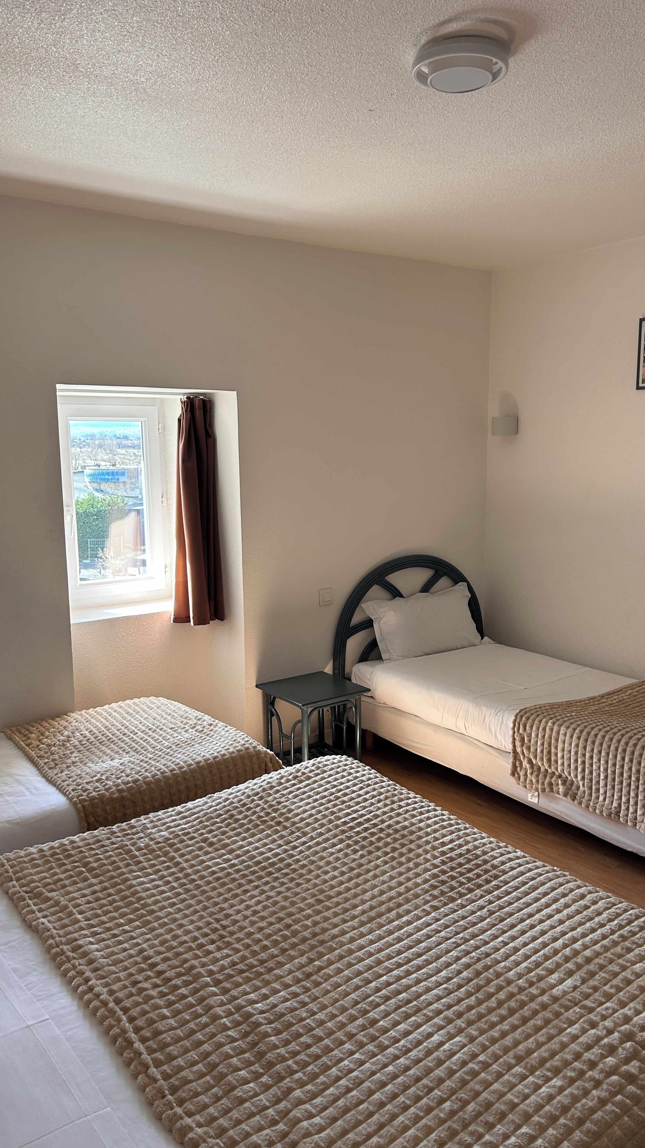 A room with two beds, a window with curtains, a small table, and a ceiling light.